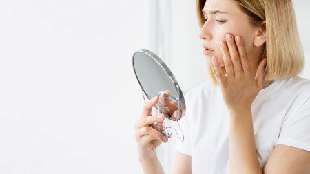 A woman examining her acne-prone skin in the mirror, pleased with the improvement by following clear skin steps.